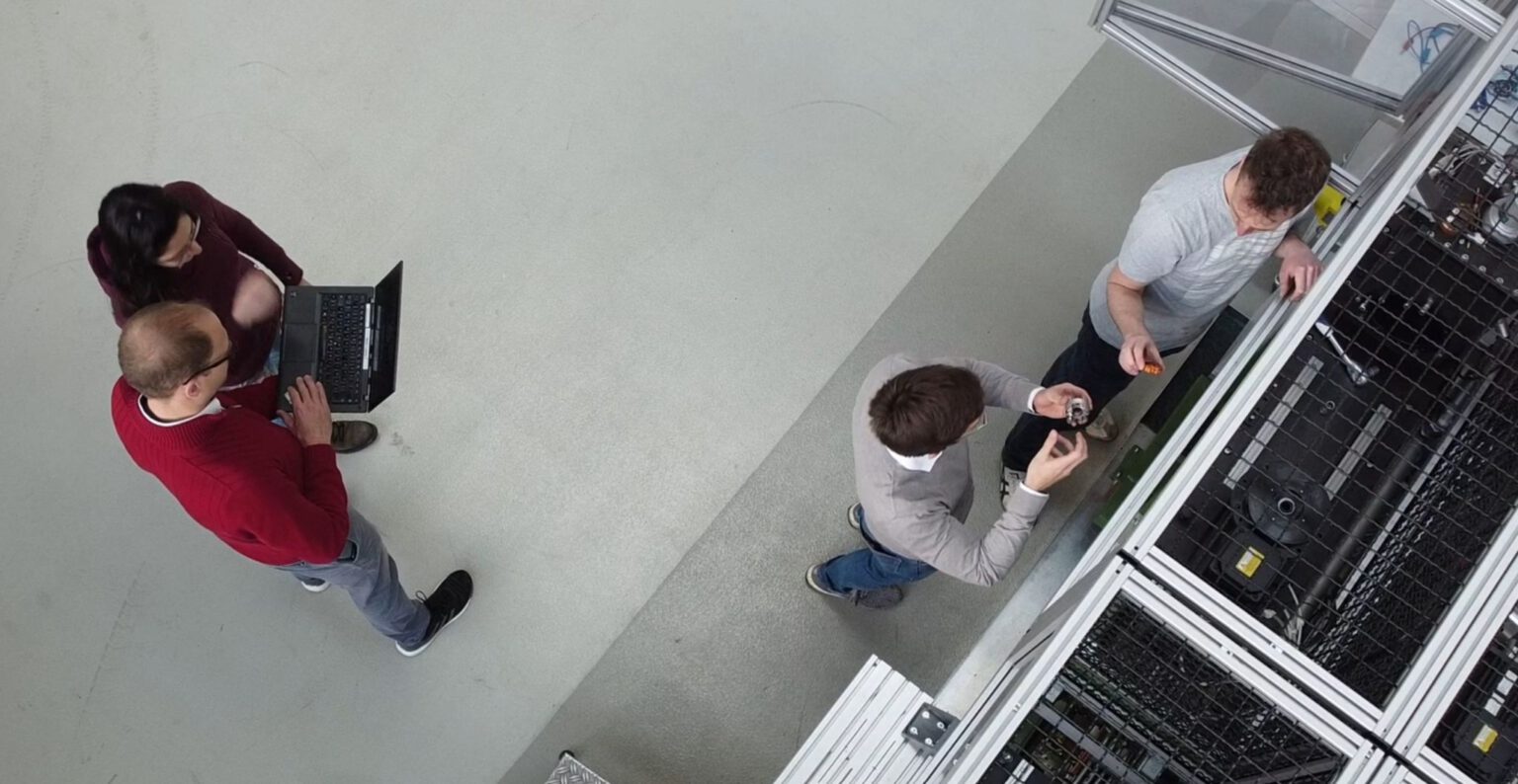 Ein Photo von der Zusammenarbeit von HCP Sense Team, das gemeinsam in der Produktionshalle vor einer Anlage arbeiten