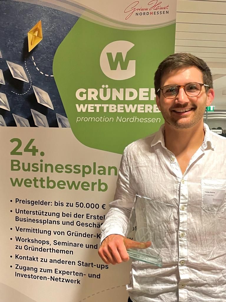 Ein Photo von HCP Sense Mitgründer vor einem Poster von dem Gründer Wettbewerb